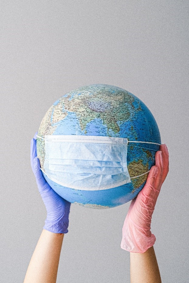 globe with a face mask held by a pair of gloved hands