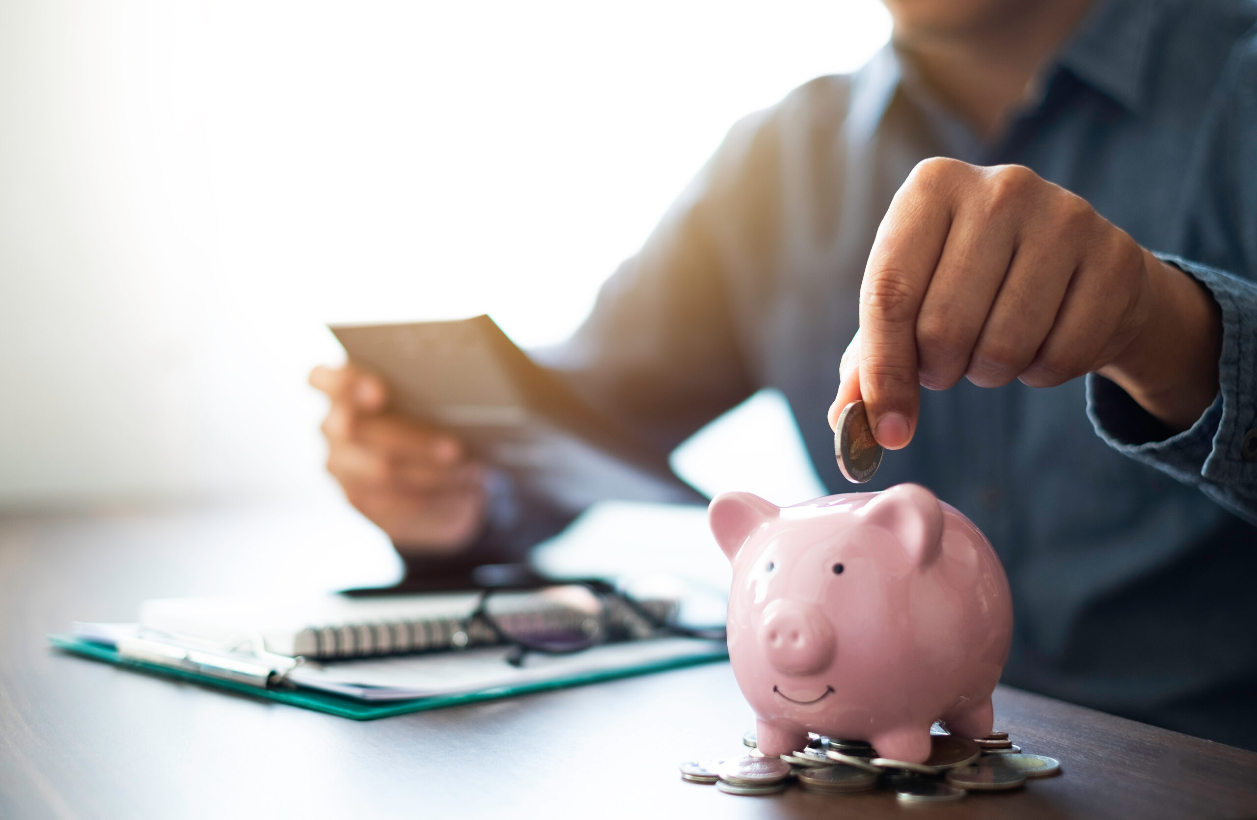 Close-up image of man hand putting coins in pink piggy bank