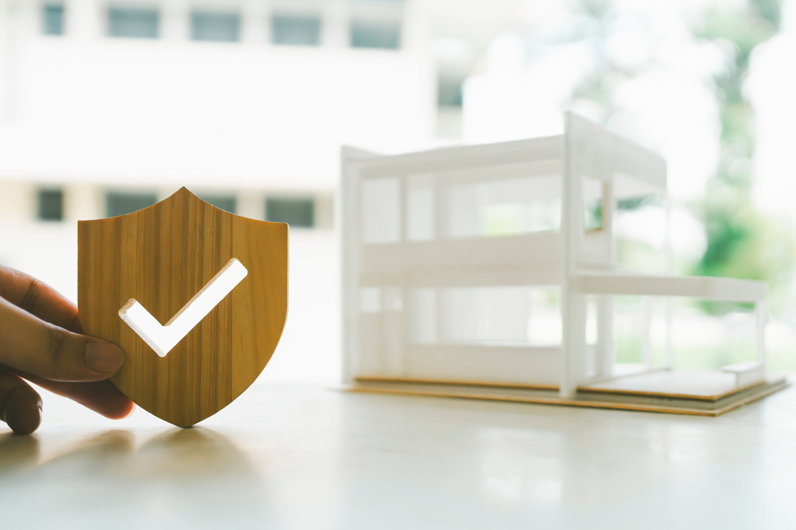 Wooden house model and real estate insurance ideas, and small shield icon.